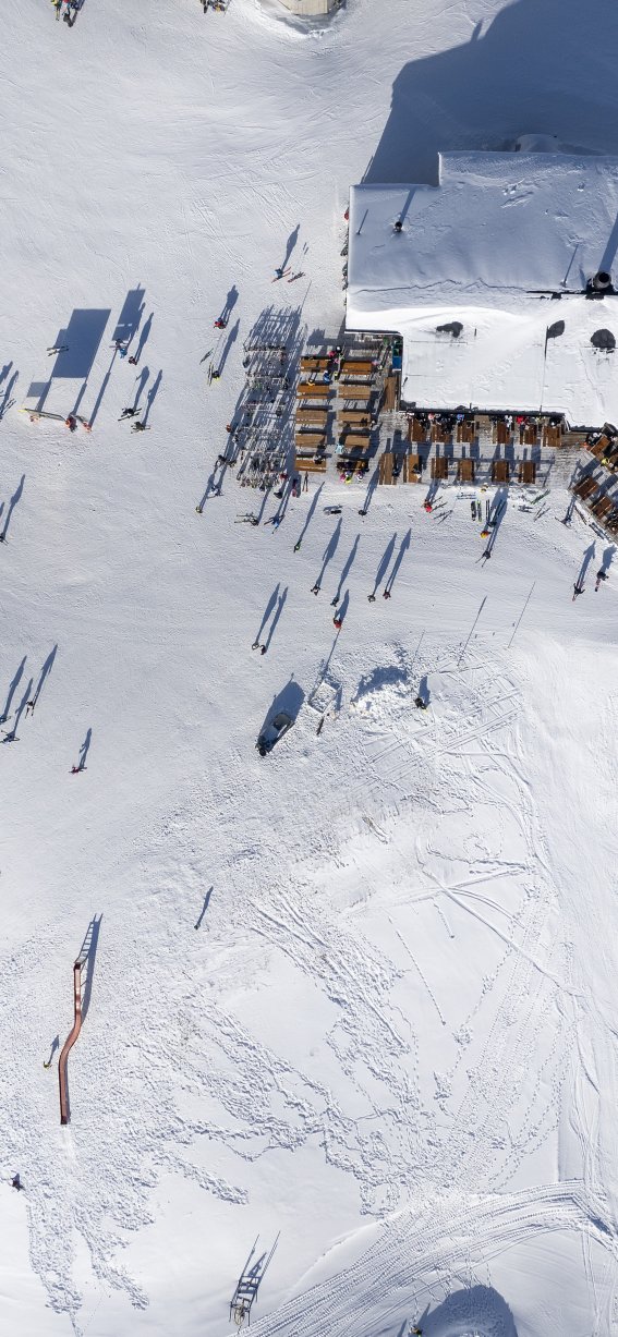 Eine belebte Szenerie in einem Skigebiet mit vielen Menschen auf dem Schnee und einem Gebäude im Hintergrund.