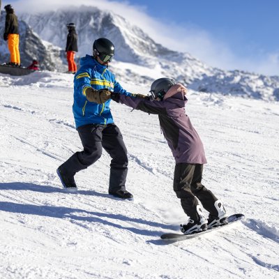 Kinder und Erwachsene üben das Snowboarden auf der Piste in den Bergen an einem sonnigen Wintertag.