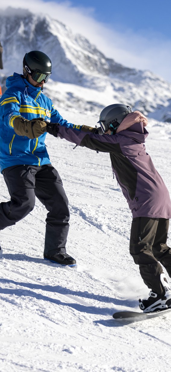 Kinder und Erwachsene üben das Snowboarden auf der Piste in den Bergen an einem sonnigen Wintertag.