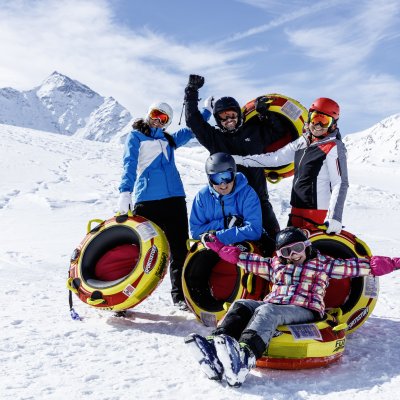 Fünf Personen lachen und genießen den Schnee, während sie mit Reifen im Winterurlaub spielen und Spaß haben.