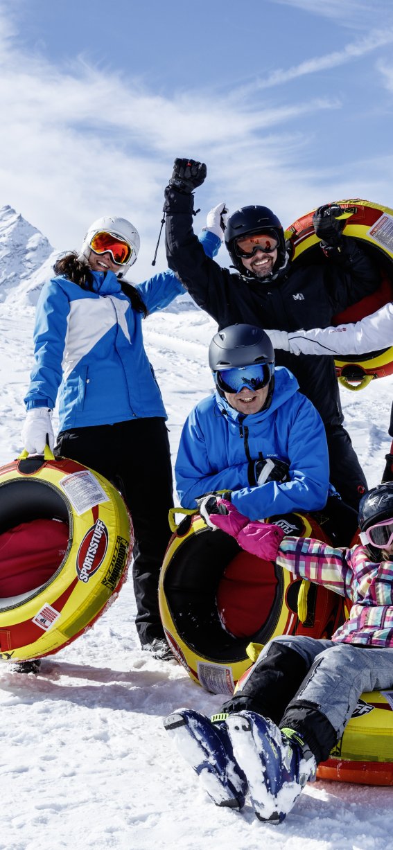 Fünf Personen lachen und genießen den Schnee, während sie mit Reifen im Winterurlaub spielen und Spaß haben.