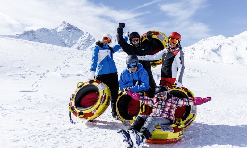 Fünf Personen lachen und genießen den Schnee, während sie mit Reifen im Winterurlaub spielen und Spaß haben.
