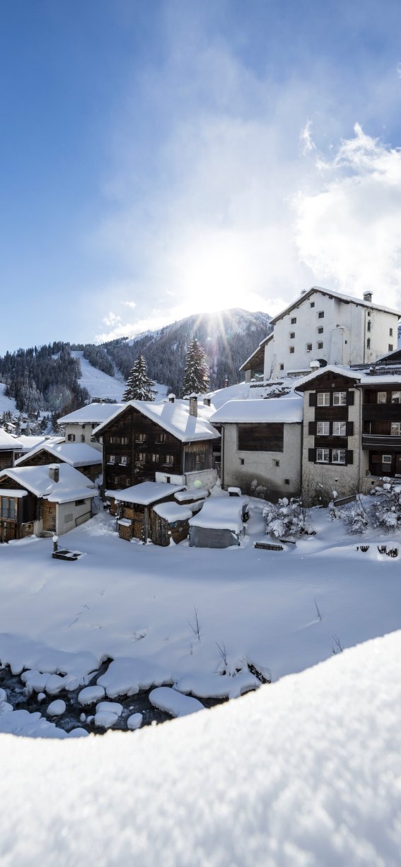 Im Sonnenlicht liegen die verschneiten Hütten friedlich im Tal und zeigen eine winterliche Landschaft in den Alpen.