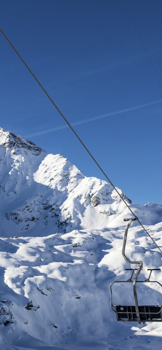 Zwei Skifahrer fahren mit dem Sessellift in den verschneiten Alpen auf einem sonnigen Tag.