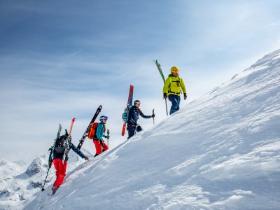 Vier Skifahrer steigen auf einen verschneiten Berg in den Alpen während eines klaren, sonnigen Tages.
