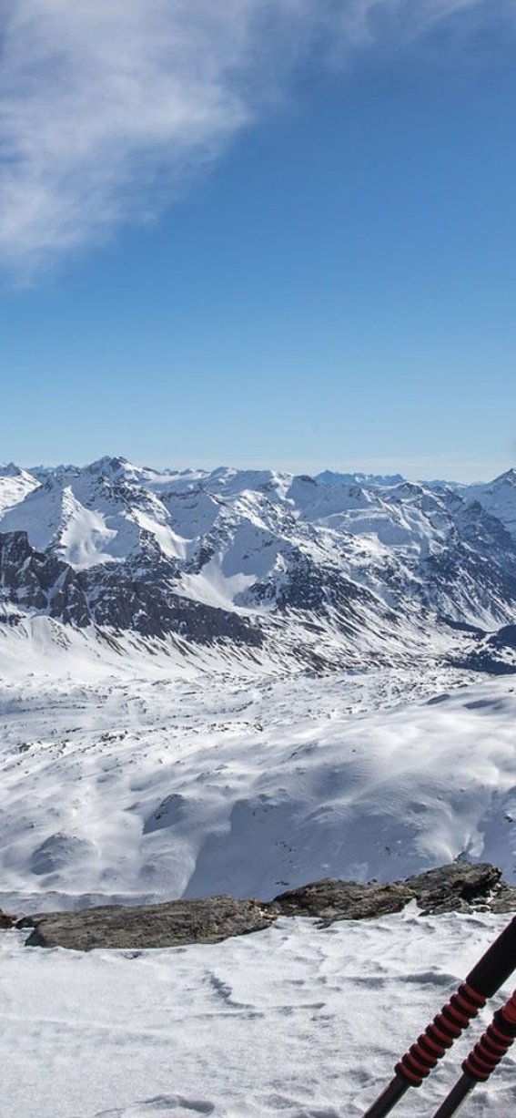 Ein Wanderer trägt eine orange Jacke und schaut auf sein Handy, während er die bergige Winterlandschaft bewundert.