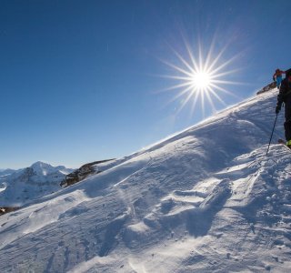 Eine Person erklimmt einen schneebedeckten Berg unter strahlendem Sonnenschein an einem klaren Wintertag.