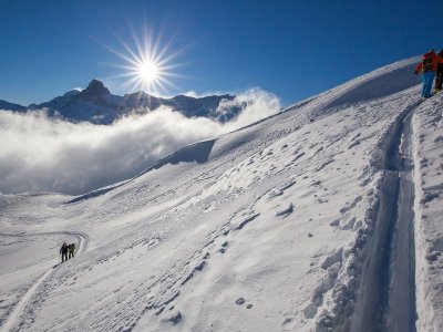 Menschen wandern auf einer schneebedeckten Fläche in den Bergen. Die Sonne scheint am klaren Himmel.