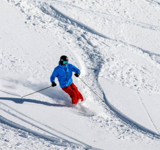 Ein Skifahrer genießt die Piste mit frischem Schnee an einem sonnigen Wintertag in den Bergen.