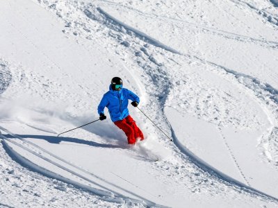 Ein Skifahrer genießt die Piste mit frischem Schnee an einem sonnigen Wintertag in den Bergen.