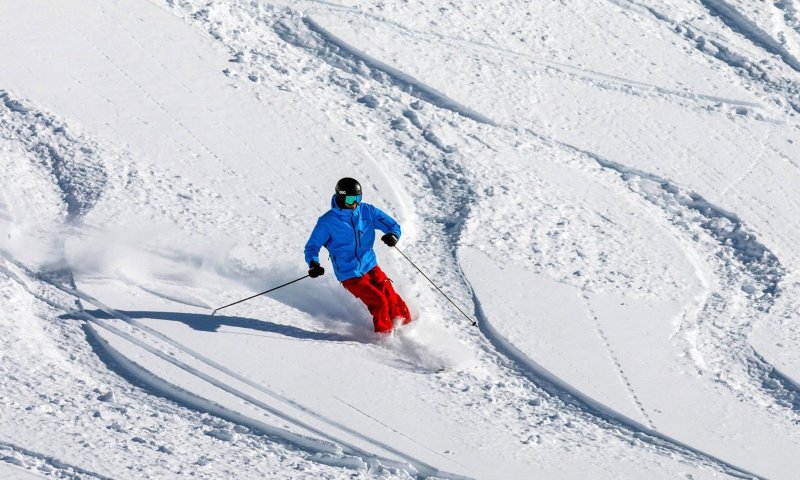 Ein Skifahrer genießt die Piste mit frischem Schnee an einem sonnigen Wintertag in den Bergen.