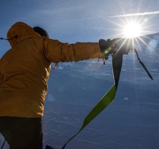 Eine Person besteigt einen schneebedeckten Hang, während die Sonne hell scheint. Die Szene zeigt einen majestätischen Berg.