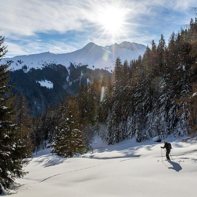 Ein abenteuerlustiger Wanderer bewegt sich durch verschneite Landschaften im Gebirge an einem sonnigen Wintertag.