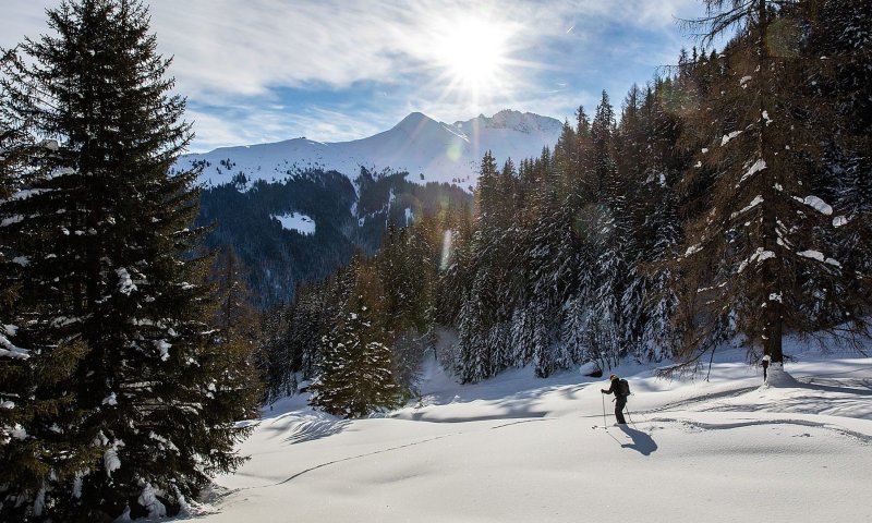 Ein abenteuerlustiger Wanderer bewegt sich durch verschneite Landschaften im Gebirge an einem sonnigen Wintertag.