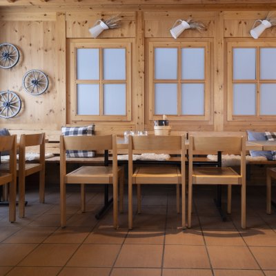 Der Innenraum zeigt Holzstühle und Tische in einem Restaurant. Fenster sind an der Wand. Es ist tagsüber.