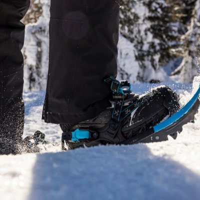 Eine Person wandert mit Schneeschuhen durch den Schnee. Die Sonne scheint und die Bäume sind mit Schnee bedeckt.
