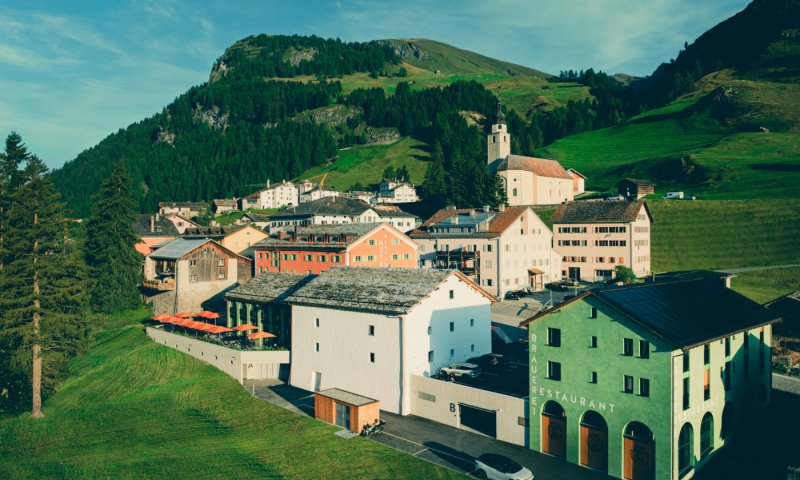 Das Dorf zeigt die Spleuca, Berge und einen klaren Himmel. Menschen verbringen Zeit draußen in einer schönen Umgebung.