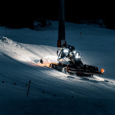Eine Pistenraupe fährt auf einer Skipiste und bereitet den Schnee für Skifahrer in der Nacht vor.