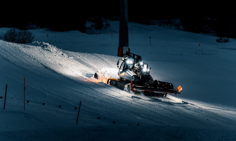 Eine Pistenraupe fährt auf einer Skipiste und bereitet den Schnee für Skifahrer in der Nacht vor.