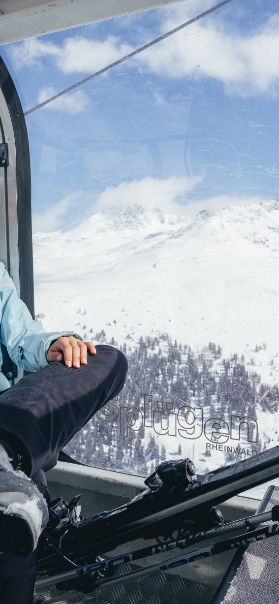 Eine Frau sitzt in einer Seilbahn und schaut auf die Schneelandschaft. Es ist eine kalte Wintersaison mit klarem Himmel.