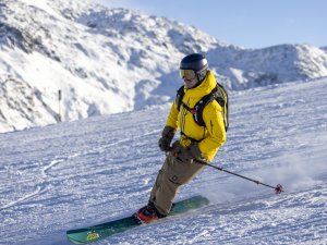 Ein Touren-Skifahrer fährt bei klarem Wetter auf einem Schnee bedeckten Hang in den Bergen.