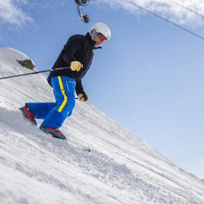 Eine Person fährt Telemark den Hang hinunter. Die Sonne scheint und der Schnee deckt die Piste.