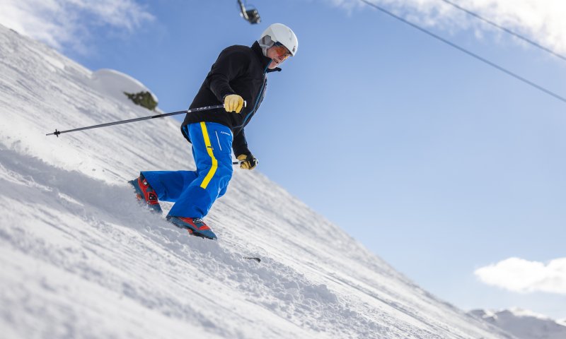 Eine Person fährt Telemark den Hang hinunter. Die Sonne scheint und der Schnee deckt die Piste.