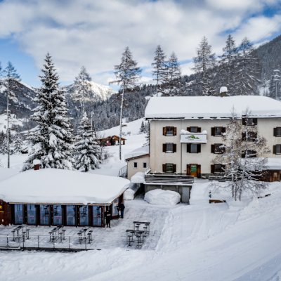 Das Bild zeigt das Gebäude Hüschera Lodge, das direkt an der Piste und neben der Hüschera Bard liegt. Die Landschaft darum ist tief verschneit.
