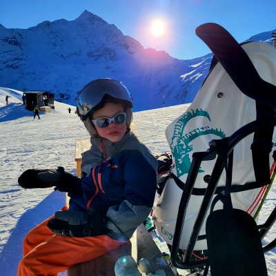 Ein Kind mit Beeinträchtigung sitzt auf einem Bänkli an der Sonne neben ihrem Dualski.