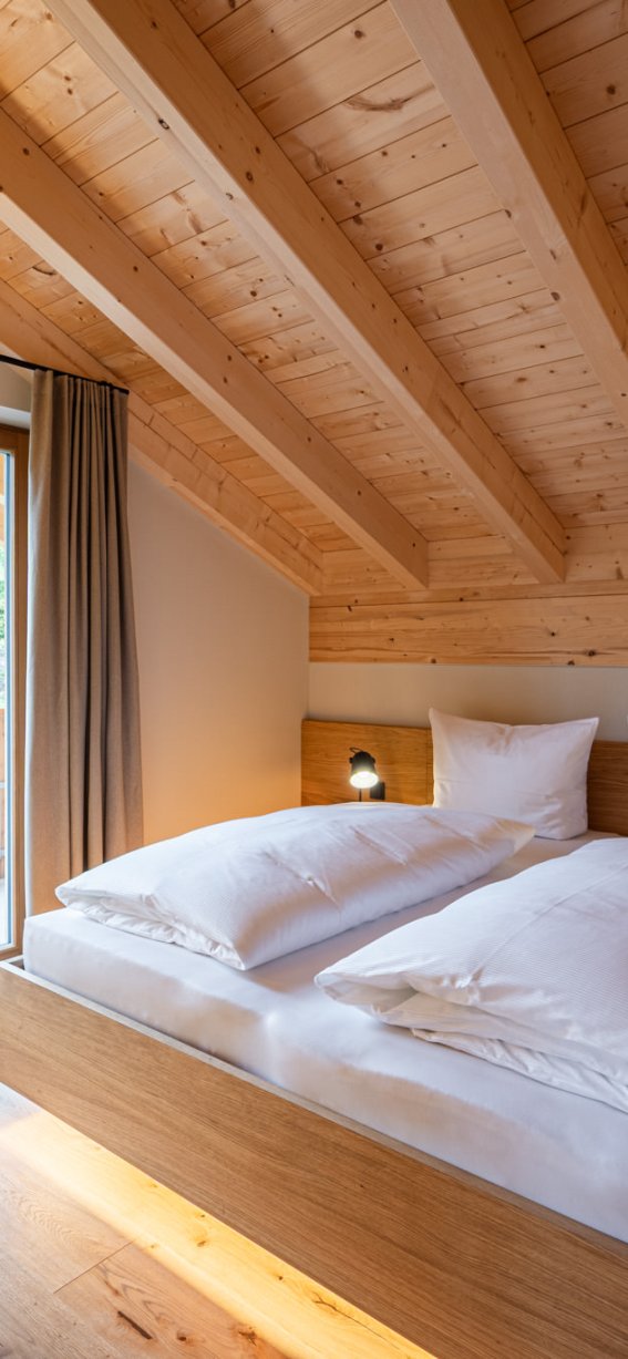 Helles Schlafzimmer mit Holzdecken und gemütlichem Doppelbett. Große Fenster bieten Blick auf die Natur.
