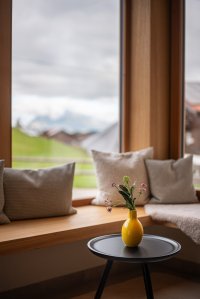 Eine helle Ecke mit einem Tisch, einer Vase und Kissen zeigt die Berge an einem bewölkten Tag.