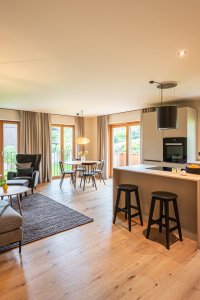 Helles und einladendes Wohnzimmer mit offener Küche in einem modernen Apartment. Große Fenster lassen viel Licht hereinfliessen.