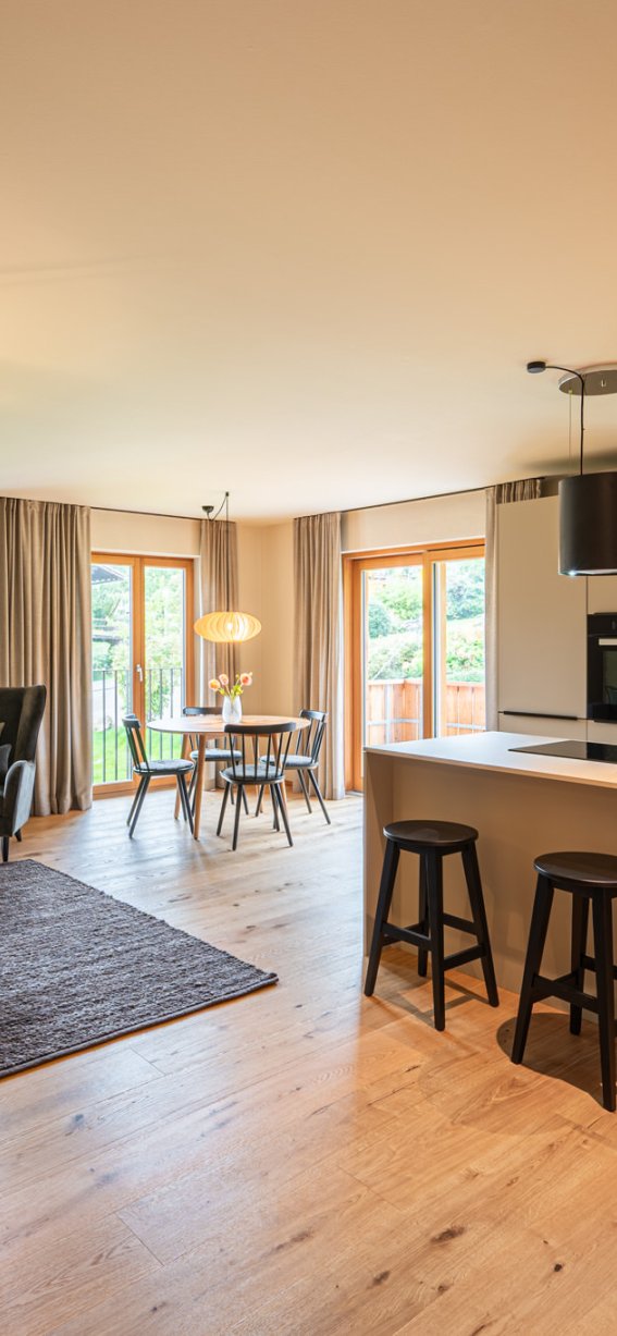 Helles und einladendes Wohnzimmer mit offener Küche in einem modernen Apartment. Große Fenster lassen viel Licht hereinfliessen.