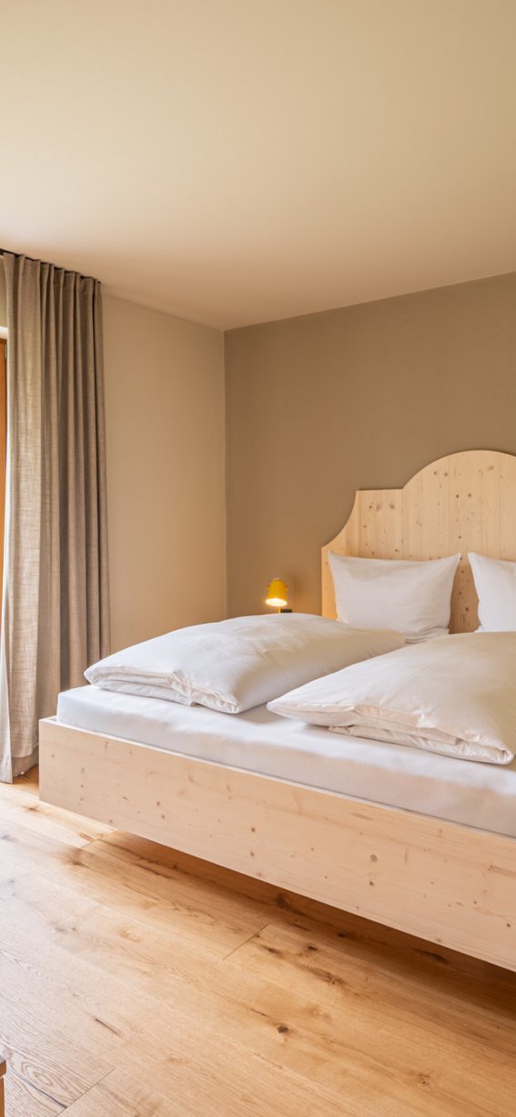 Helles Schlafzimmer mit Doppelbett und Balkonblick. Holzfußboden und sanfte Beleuchtung schaffen eine einladende Atmosphäre.