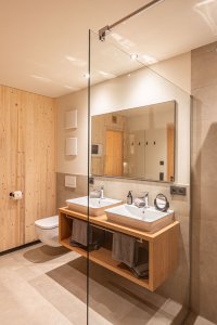 Helles Badezimmer mit Holzverkleidung, Doppelwaschbecken, Dusche und modernen Armaturen.