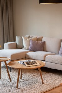 In einem hellen Raum steht ein bequemes Sofa neben einem Tisch. Draußen ist eine Terrasse sichtbar.