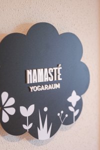 Ein schöner Schild zeigt den Yogaraum mit dem Namen Namasté. Die floral gestaltete Tafel hängt an einer Wand.