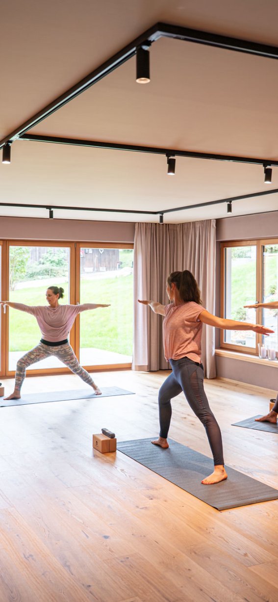 Vier Personen üben Yoga in einem modernen Raum mit großen Fenstern. Der Kurs findet tagsüber statt.