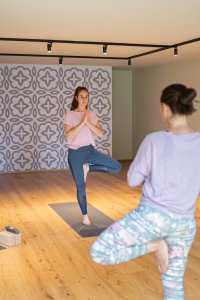 Vier Frauen üben Yoga in einem hellen Raum mit Holzboden und dekorativen Wänden.