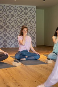 Vier Frauen praktizieren Atemübungen während einer Yoga-Klasse in einem ruhigen Studio mit Holzfußboden.