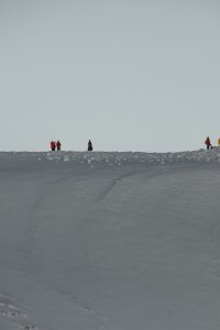 Wanderer bewegen sich auf einer hohen, schneebedeckten Bergspitze an einem klaren Tag in den Alpen.