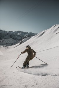 Ein Skifahrer gleitet über die schneebedeckte Piste in den Bergen an einem klaren, sonnigen Tag.