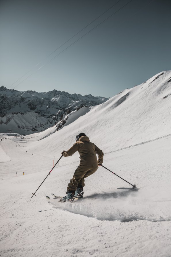 Ein Skifahrer gleitet über die schneebedeckte Piste in den Bergen an einem klaren, sonnigen Tag.