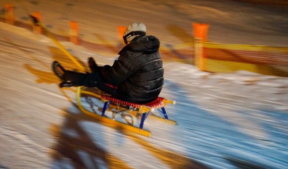 Ein Schlittenfahrer gleitet rasch den verschneiten Hang hinunter. Die Nacht ist klar und die Stimmung ist aufregend.