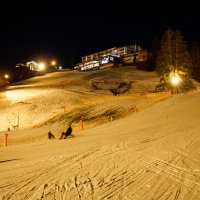 Skifahrer genießen die Abfahrt auf einer beleuchteten Piste in einem Ski-Resort während der Nacht.