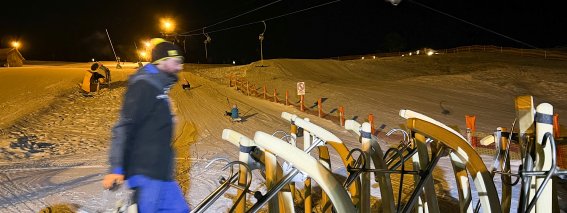 Ein Mann bereitet den Skilift für die nächtliche Skiaktivität in den Alpen vor. Die Pisten sind mit Schnee bedeckt und beleuchtet.
