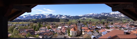 Ausblick Balkon Himmeleck II Die Aussicht zeigt ein Dorf mit einem weißen Kirchengebäude. Umgeben von Bergen an einem sonnigen Tag. Es zeigt den Ausblick vom Balkon der Wohnung Himmeleck.