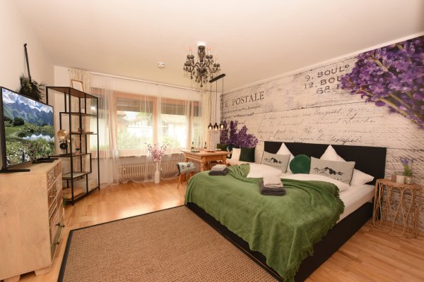 Das Zimmer hat ein großes Bett und einen Fernseher. Es gibt Pflanzen und eine gemütliche Atmosphäre im Raum.