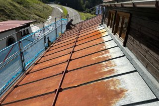 Renovierung des Daches in den Bergen Handwerker sanieren das Blechdach der Walserschanz an einem sonnigen Tag.