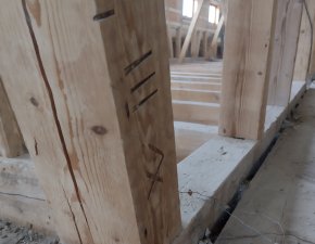 Der Holzpfosten steht in einem Rohbau. Baustellenmaterial ist auf dem Boden verteilt. Handwerker arbeiten in der Nähe.